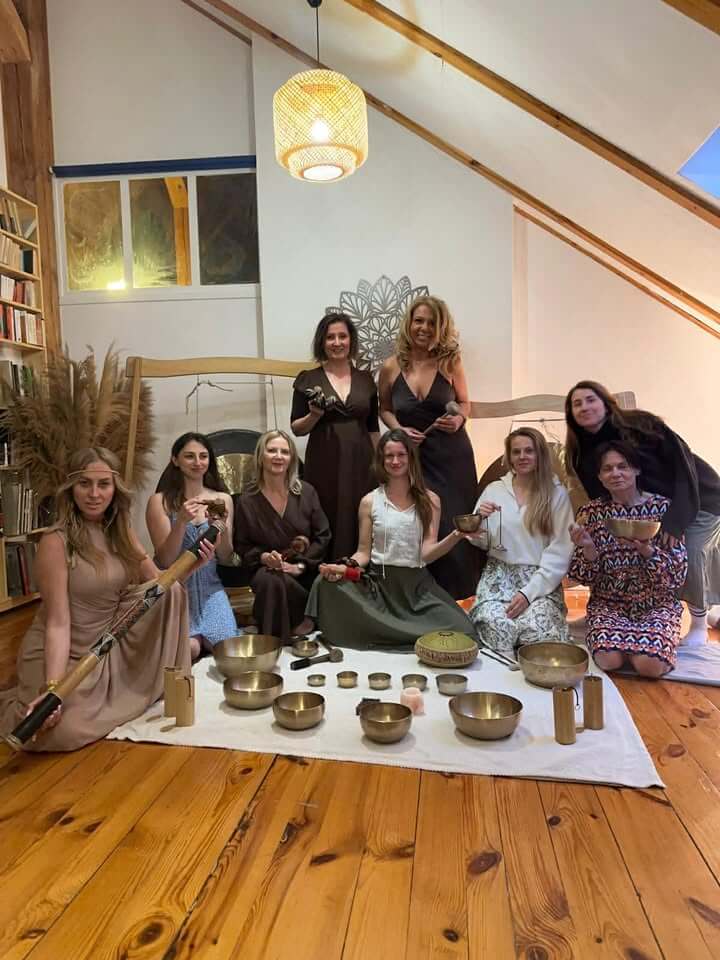 Wieczór z dźwiękiem (sound healing) – grupa uczestniczek pozuje na drewnianej podłodze wokół rozłożonych mis tybetańskich, didgeridoo i innych instrumentów, w przytulnej sali z wiklinową lampą i trawą pampasową